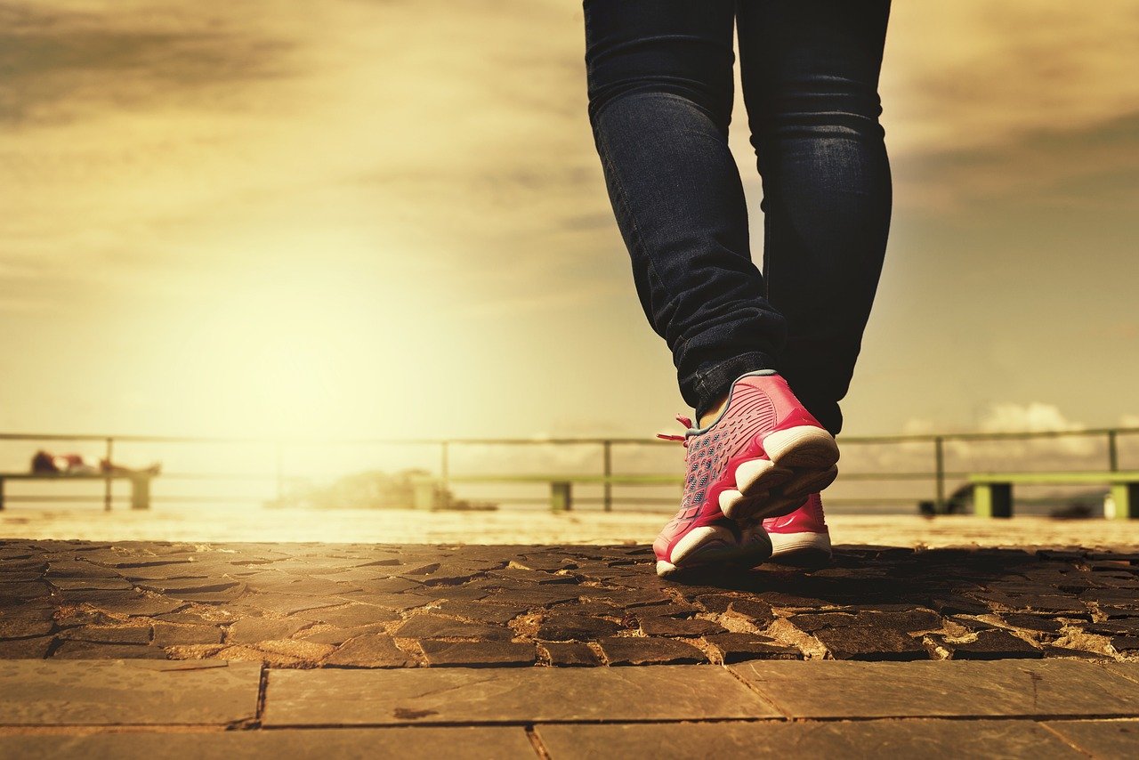 A person walking outdoors wearing pink athletic shoes during sunrise or sunset.