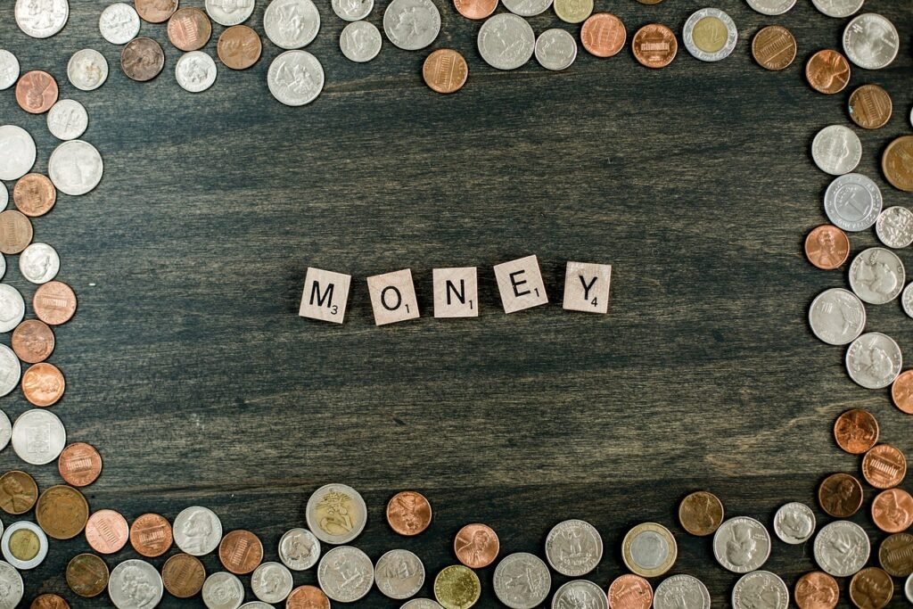 A wooden surface bordered by scattered coins, with Scrabble tiles spelling the word "MONEY" in the center